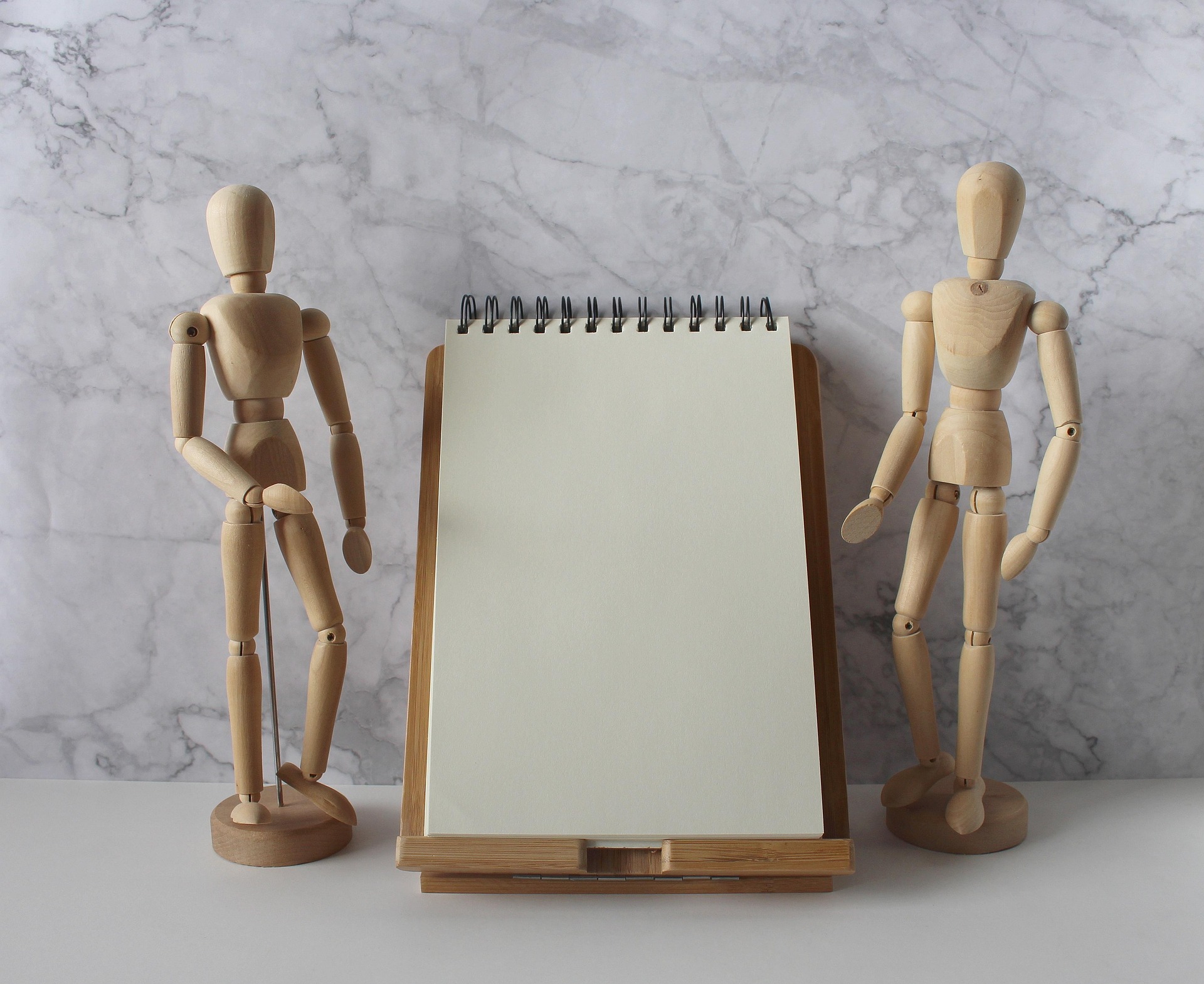 zwei Holzfiguren stehen nebeneinander, zwischen ihnen befindet sich ein leer Schreibblock